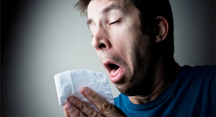 Hombre estornudando con un pañuelo de papel frente al rostro.