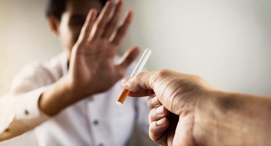 Primer plano de una mano ofreciendo un cigarrillo a un hombre que hace un gesto de rechazo con la mano, representando la decisión de dejar de fumar.