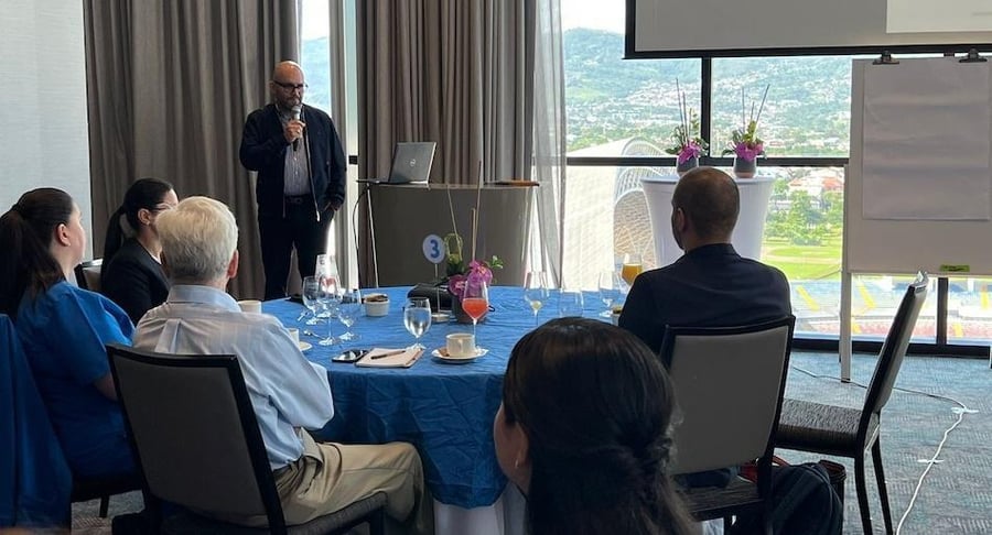 Exposición ante colaboradores del Hospital Clínica Bíblica durante una sesión informativa sobre sostenibilidad en un salón con mesas redondas.