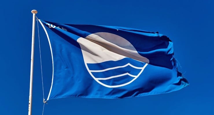 Bandera Azul Ecológica ondeando contra un cielo despejado, representando el galardón obtenido por el Hospital Clínica Bíblica por sus acciones ambientales.