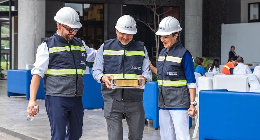 Colaboradores del Hospital Clínica Bíblica con cascos de seguridad sosteniendo una Biblia durante el acto de colocación en una obra en construcción.