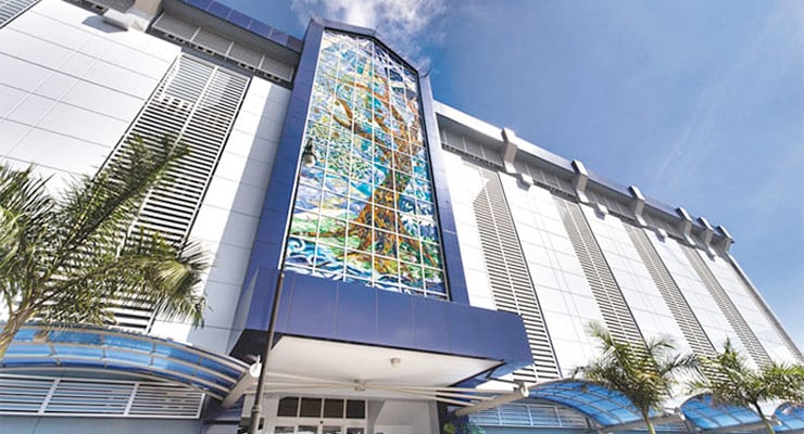 Fachada del Hospital Clínica Bíblica con ventanal artístico y palmeras al frente.