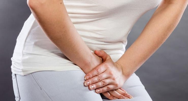 Mujer sentada sujetando la parte baja del abdomen con ambas manos por molestia