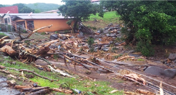 Zona residencial afectada por inundación con lodo, troncos y escombros alrededor de viviendas.