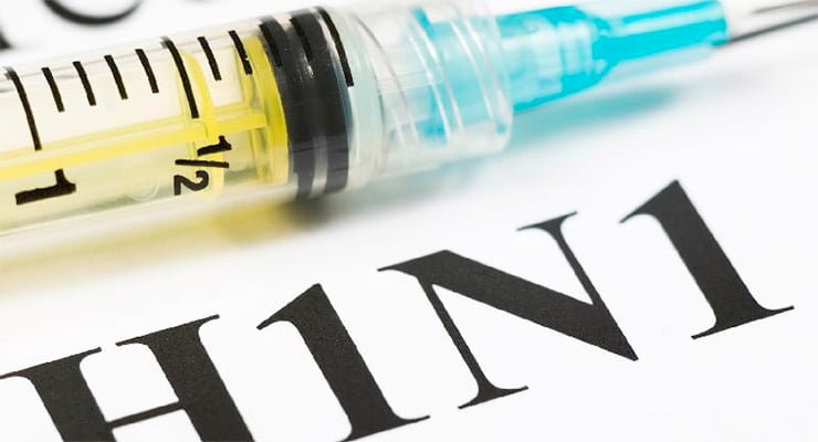 Jeringa médica colocada sobre un fondo con el texto H1N1 en primer plano.