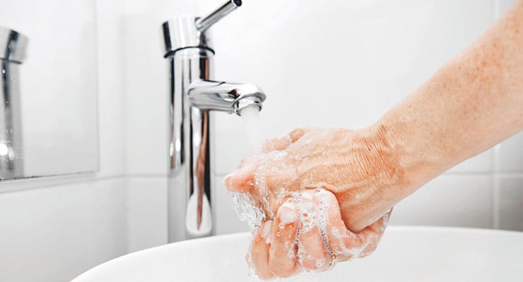 Persona lavándose las manos con agua y jabón en un lavamanos.