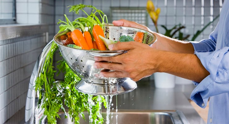 Persona lavando zanahorias y verduras frescas bajo el chorro de agua en el fregadero