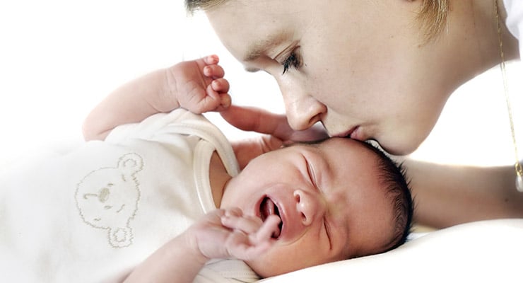 Madre besando la frente de su bebé recién nacido mientras llora