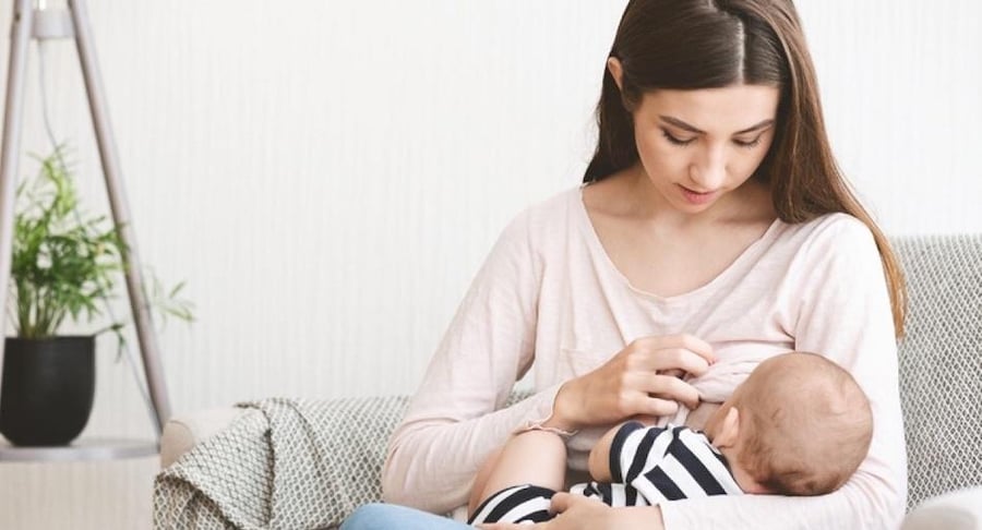 Madre joven sentada en un sillón amamantando a su bebé recién nacido con una técnica de agarre correcta y cómoda.