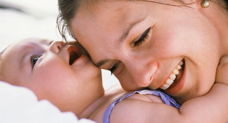 Madre sonriente recostada junto a su bebé mientras interactúan