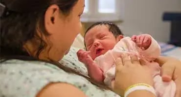 Madre sosteniendo a su recién nacida en una habitación de hospital.