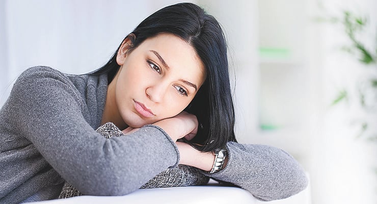 Mujer recostada con gesto pensativo y expresión de malestar emocional en un ambiente interior.