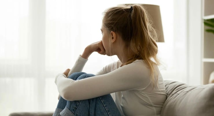 Mujer sentada en sofá mirando hacia la ventana en actitud pensativa