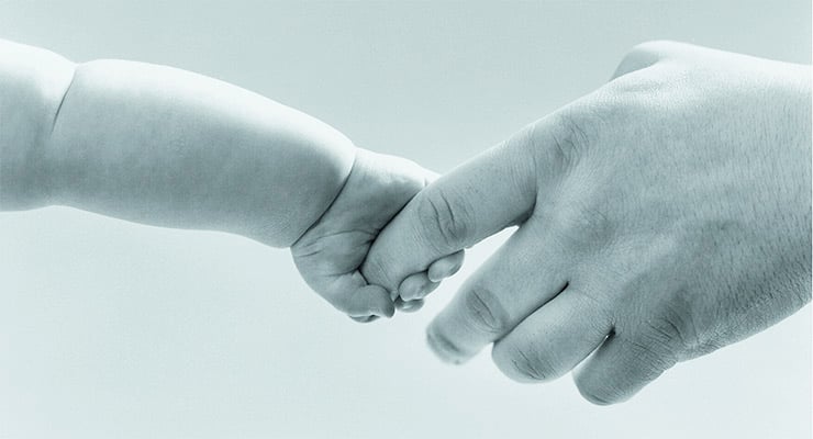 Mano de un adulto sosteniendo la mano de un bebé.
