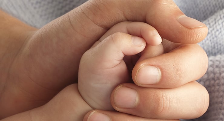 Mano de un adulto sosteniendo suavemente la mano de un bebé