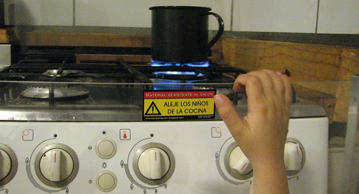 Mano de un niño cerca de una cocina encendida con una olla sobre la estufa