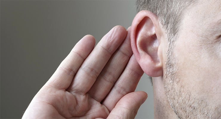 Persona acercando la mano a la oreja en gesto de escucha o atención auditiva.