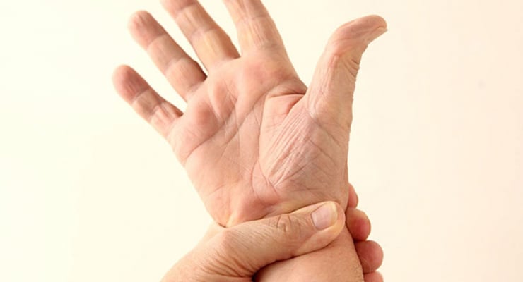 Mano abierta con la piel tensa mientras otra mano sujeta la muñeca