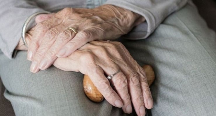 Primer plano de las manos entrelazadas de una persona adulta mayor descansando sobre su regazo, representando el proceso natural del envejecimiento.