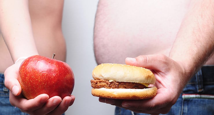 Persona sosteniendo una manzana en una mano y una hamburguesa en la otra
