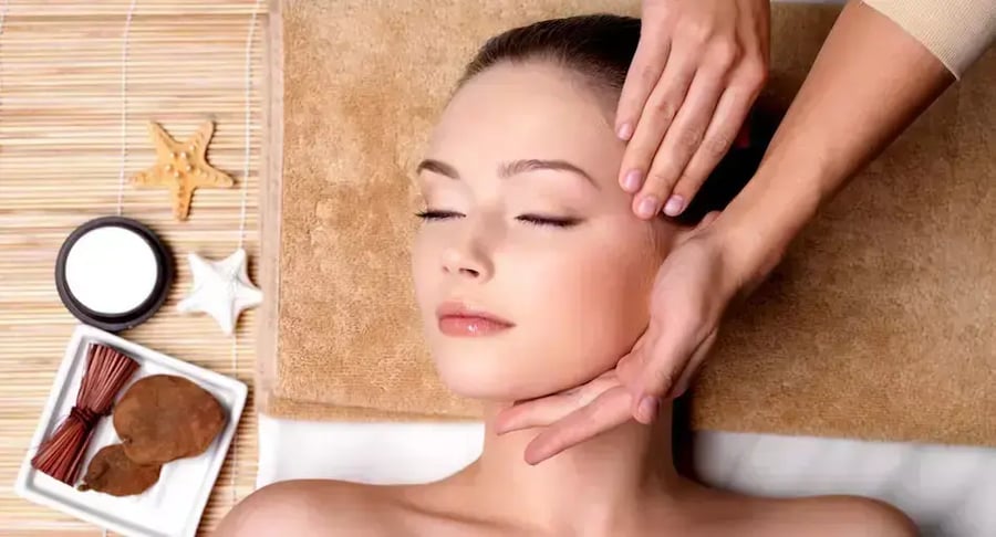Mujer recibiendo masaje facial relajante en spa con productos de cuidado de la piel
