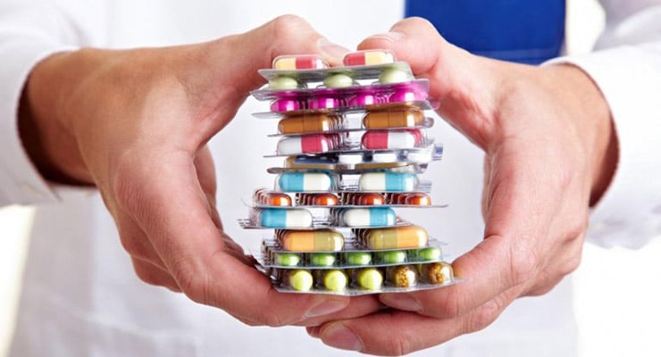 Manos sosteniendo varios blísteres de medicamentos con pastillas de distintos colores y tamaños.
