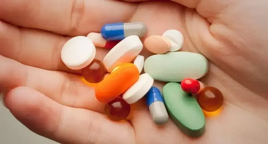 Mano sosteniendo diferentes pastillas y cápsulas de medicamentos de varios colores
