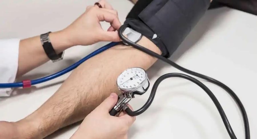 Primer plano de un profesional de la salud utilizando un esfigmomanómetro manual para medir la presión arterial en el brazo de un paciente.