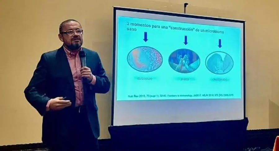 Médico de pie dando una presentación con un micrófono junto a una pantalla proyectada