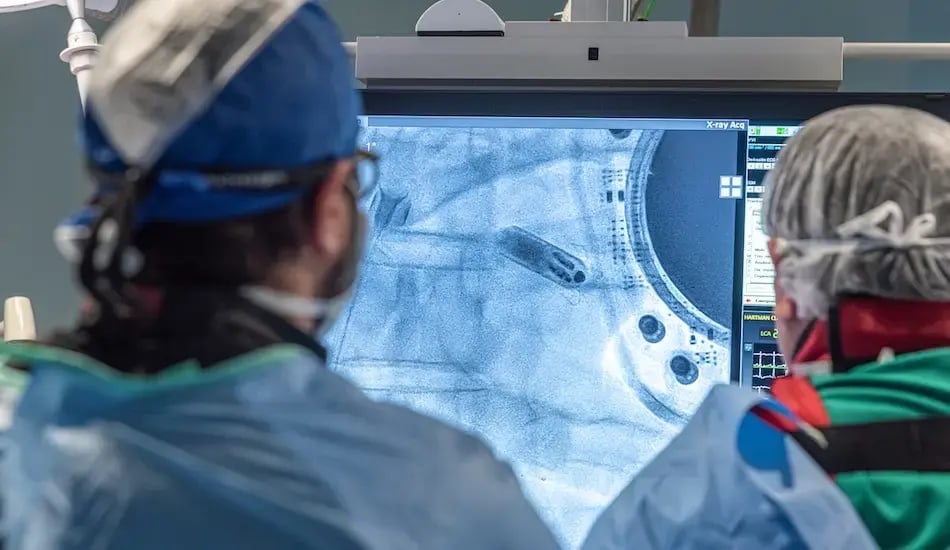 Dos profesionales de salud observan una imagen radiológica en un monitor dentro de una sala médica.
