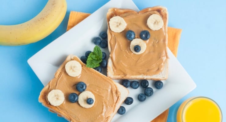 Merienda infantil con pan integral, mantequilla de maní y frutas en forma decorativa