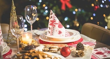 Mesa decorada para cena navideña con platos, copas, velas y adornos festivos