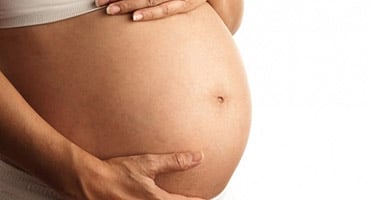 Primer plano del vientre de una mujer embarazada en avanzado estado de gestación, representando las opciones de parto y maternidad.