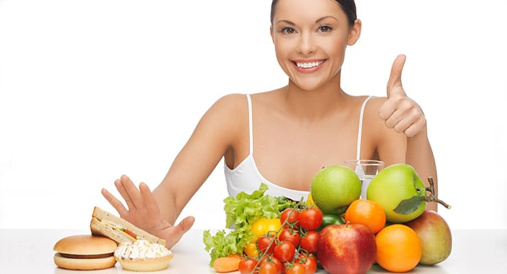 Mujer sonriente mostrando alimentos frescos y retirando comida rápida con la mano