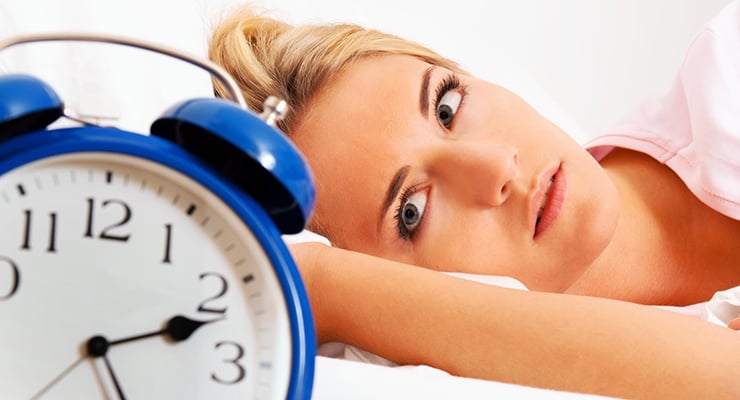 Mujer recostada en una cama junto a un reloj despertador