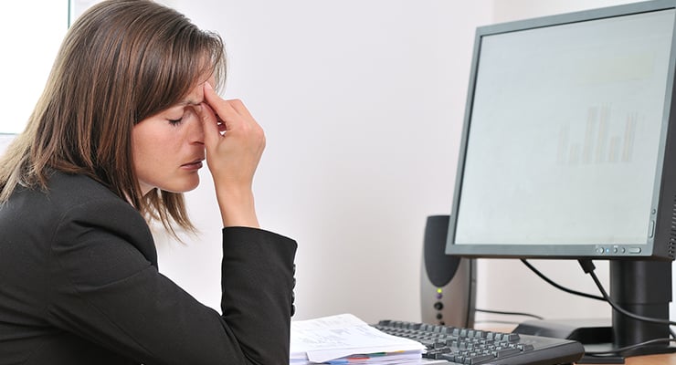 Mujer sentada frente a una computadora con la mano en la frente