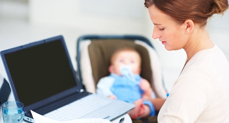 Mujer trabajando con una computadora portátil mientras un bebé permanece en una silla infantil
