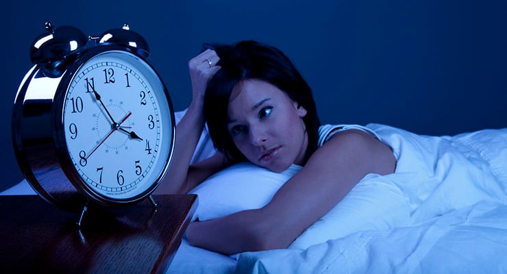 Mujer despierta en la cama mirando un reloj despertador durante la noche
