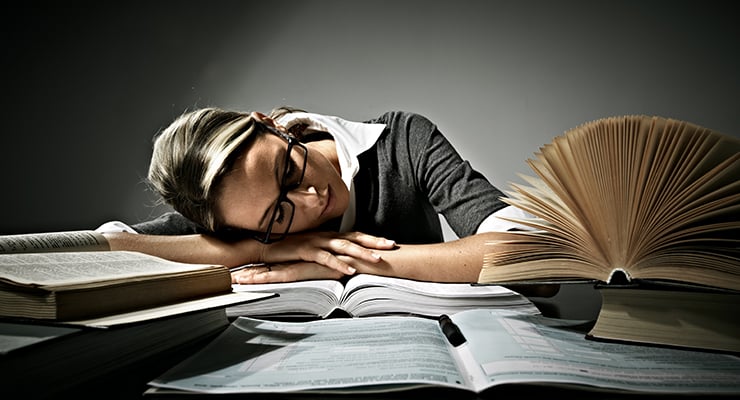 Mujer dormida sobre un escritorio con varios libros abiertos