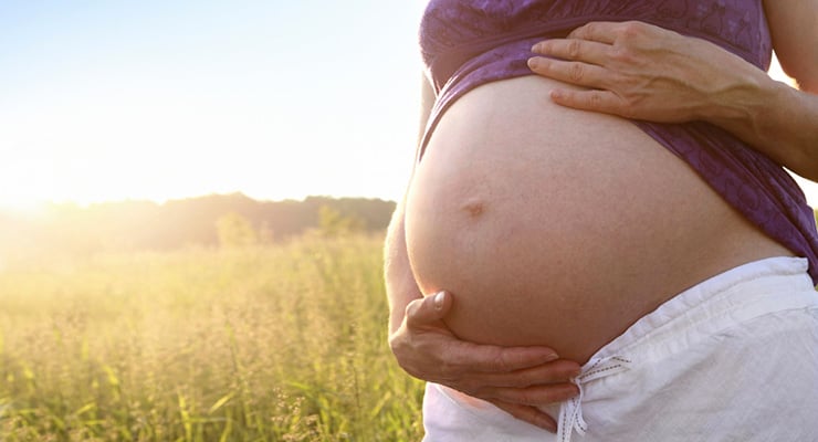 Mujer embarazada sosteniendo su abdomen con ambas manos en un entorno al aire libre