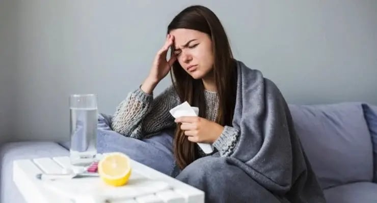 Mujer enferma en casa con fiebre y dolor de cabeza cubierta con manta