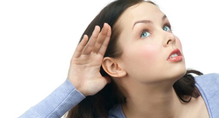 Mujer inclinando la cabeza y colocando la mano detrás de la oreja como gesto de escuchar.