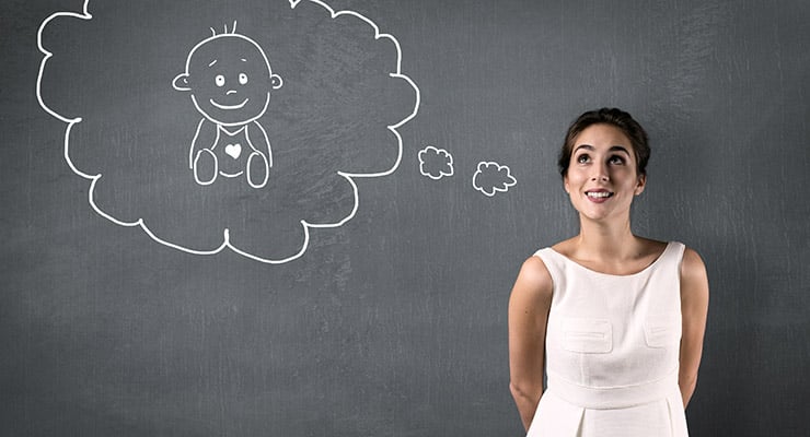 Mujer de pie mirando un dibujo de un bebé dentro de un globo de pensamiento en una pared