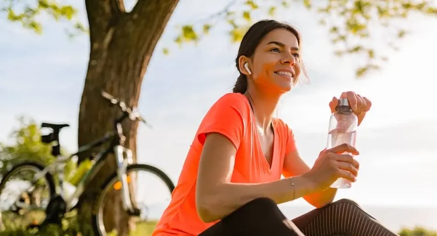 Mujer deportista descansando al aire libre con bicicleta e hidratándose con agua