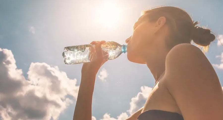 Mujer joven hidratándose con agua de botella bajo el sol para cuidar su salud