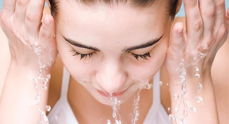 Mujer lavándose el rostro con agua, realizando limpieza facial con ambas manos.