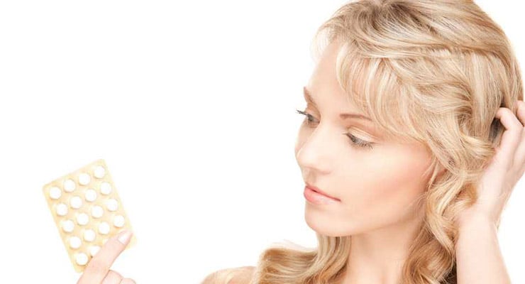 Mujer observando un blíster de pastillas anticonceptivas que sostiene con la mano.