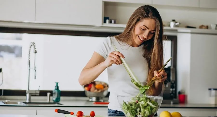 Mujer joven preparando una ensalada saludable en la cocina para prevenir diabetes