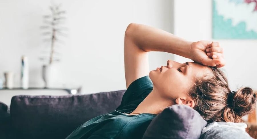 Mujer joven recostada en un sofá con el brazo sobre la frente mostrando signos de agotamiento mental y ansiedad