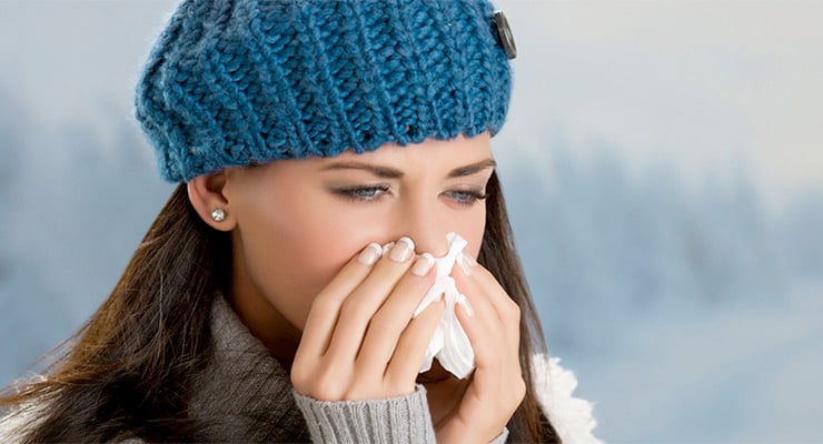 Mujer con gorro de lana cubriéndose la nariz con un pañuelo, mostrando síntomas de resfriado o gripe.